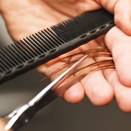 Close-up of a stylist holding a comb and scissors through a section of hair